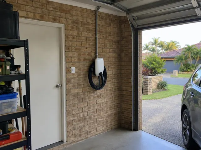 Wall-mounted EV charger on a brick garage wall beside a door and driveway in Robina