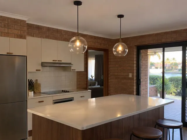 Kitchen with two glass pendant lights over a stone island and brick walls in Burleigh Waters