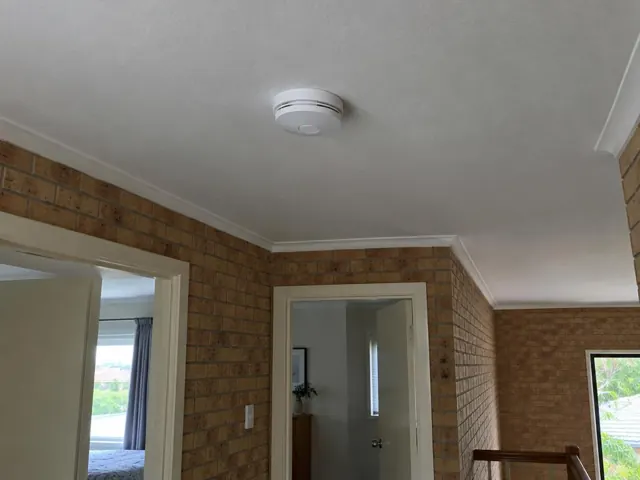 Ceiling smoke alarm in a brick hallway with doorways and white trim in Varsity Lakes